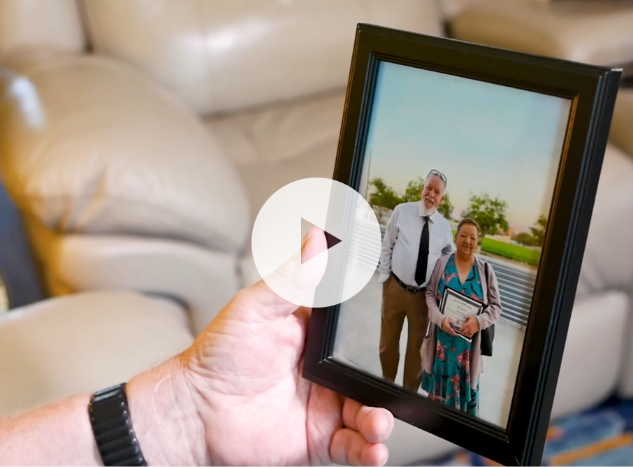 Over-the-shoulder perspective photo of a man holding a framed picture. A play button is overlaid on top.