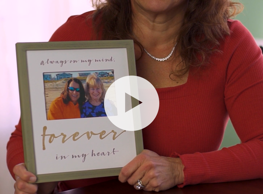 Photo of a woman holding up a framed picture. A play button is overlaid on top.